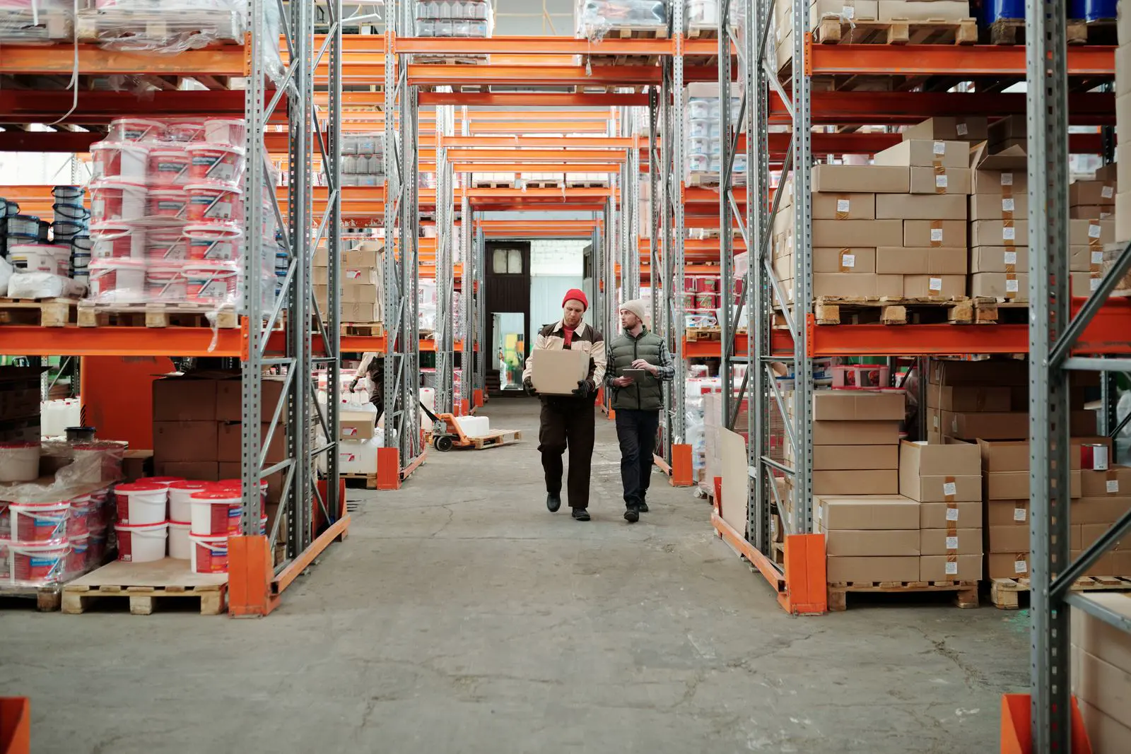 Warehouse aisles with racked pallets and two staff walking